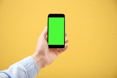 Man holding smartphone with green screen on yellow background, closeup. Gadget display with chroma key. Mockup for design