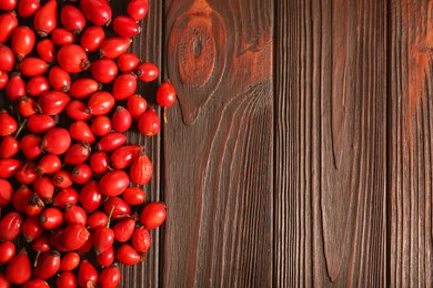 Photo of Fresh ripe rosehip berries on wooden table, flat lay. Space for text