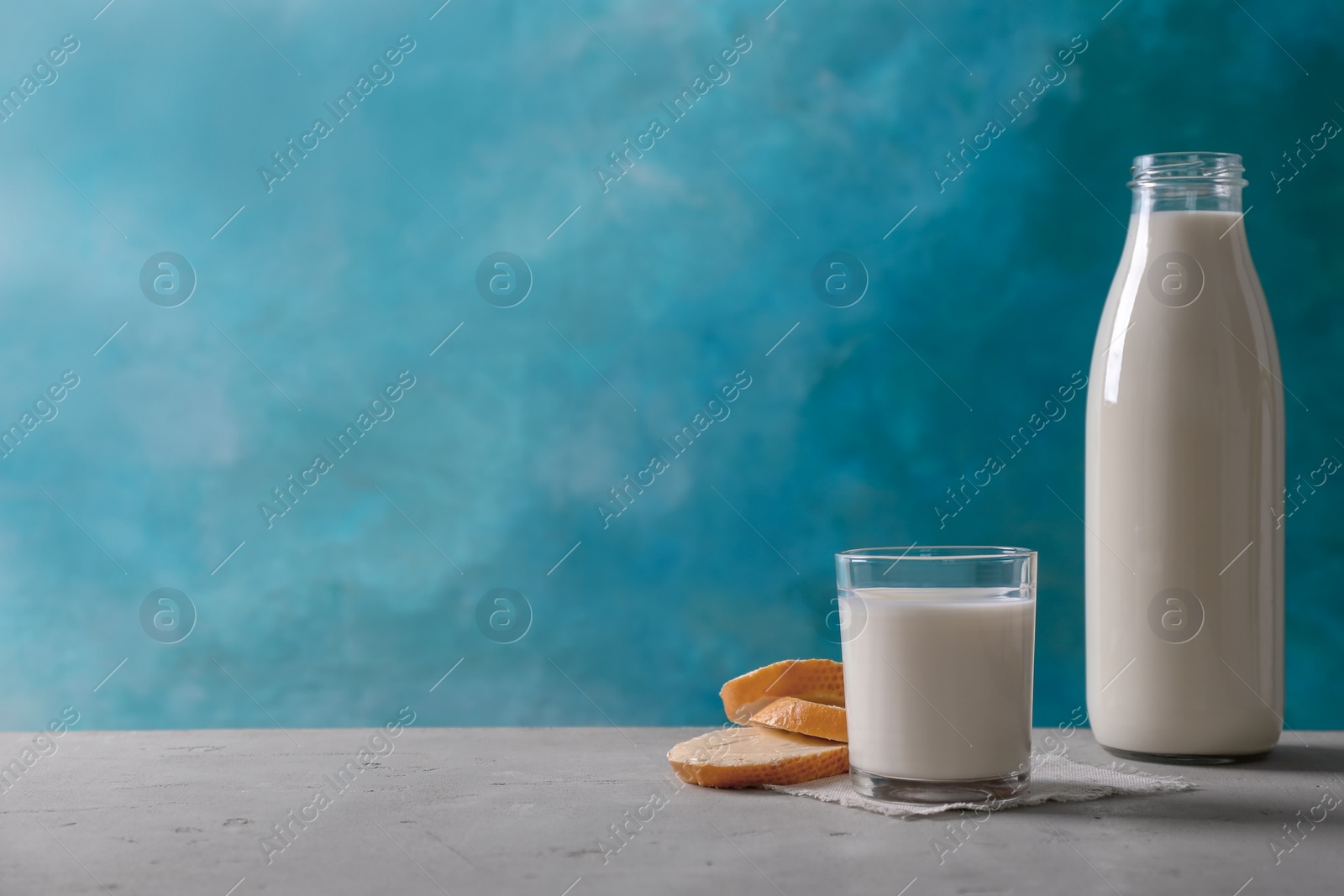 Photo of Glassware with milk and bread on table against color background