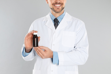 Photo of Professional pharmacist with syrup on light grey background, closeup