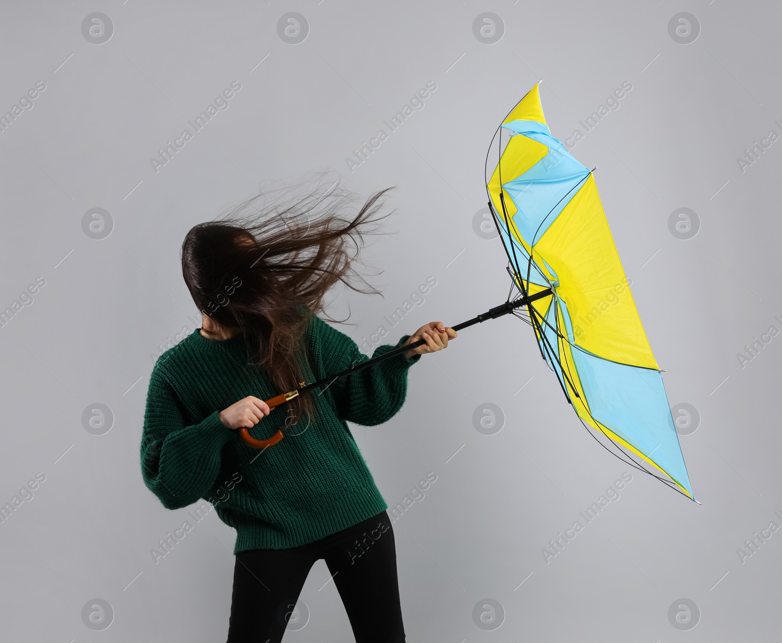 Photo of Woman with umbrella caught in gust of wind on grey background