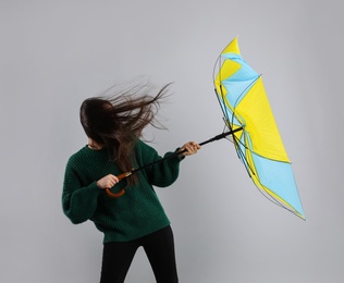 Photo of Woman with umbrella caught in gust of wind on grey background