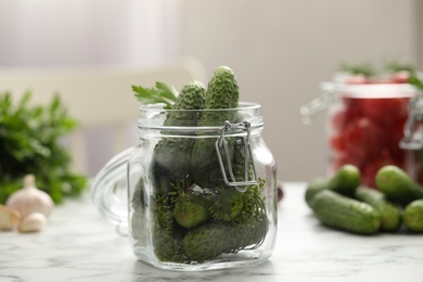 Pickling jar with fresh cucumbers on white marble table