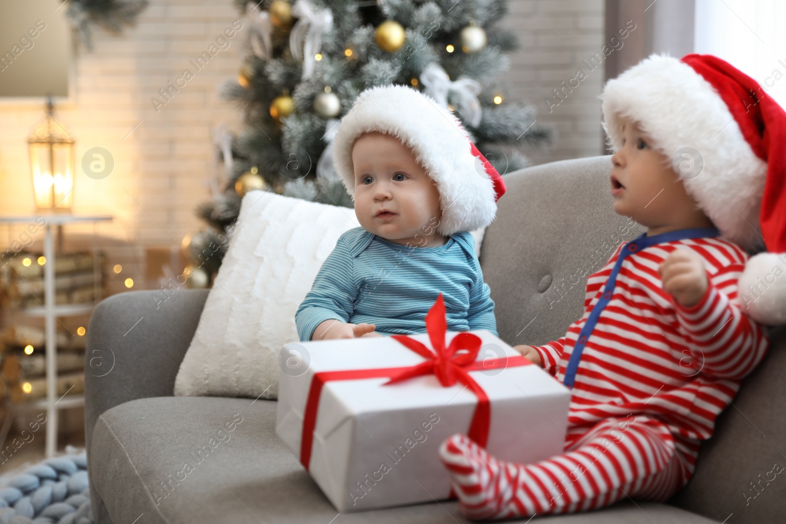 Image of Cute children in Santa hats sitting on sofa at home. Christmas celebration