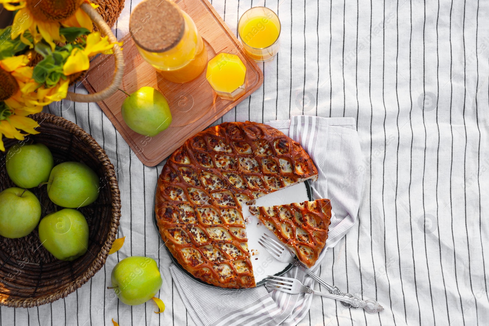 Photo of Delicious pie, apples and juice on striped blanket outdoors, flat lay. Picnic season