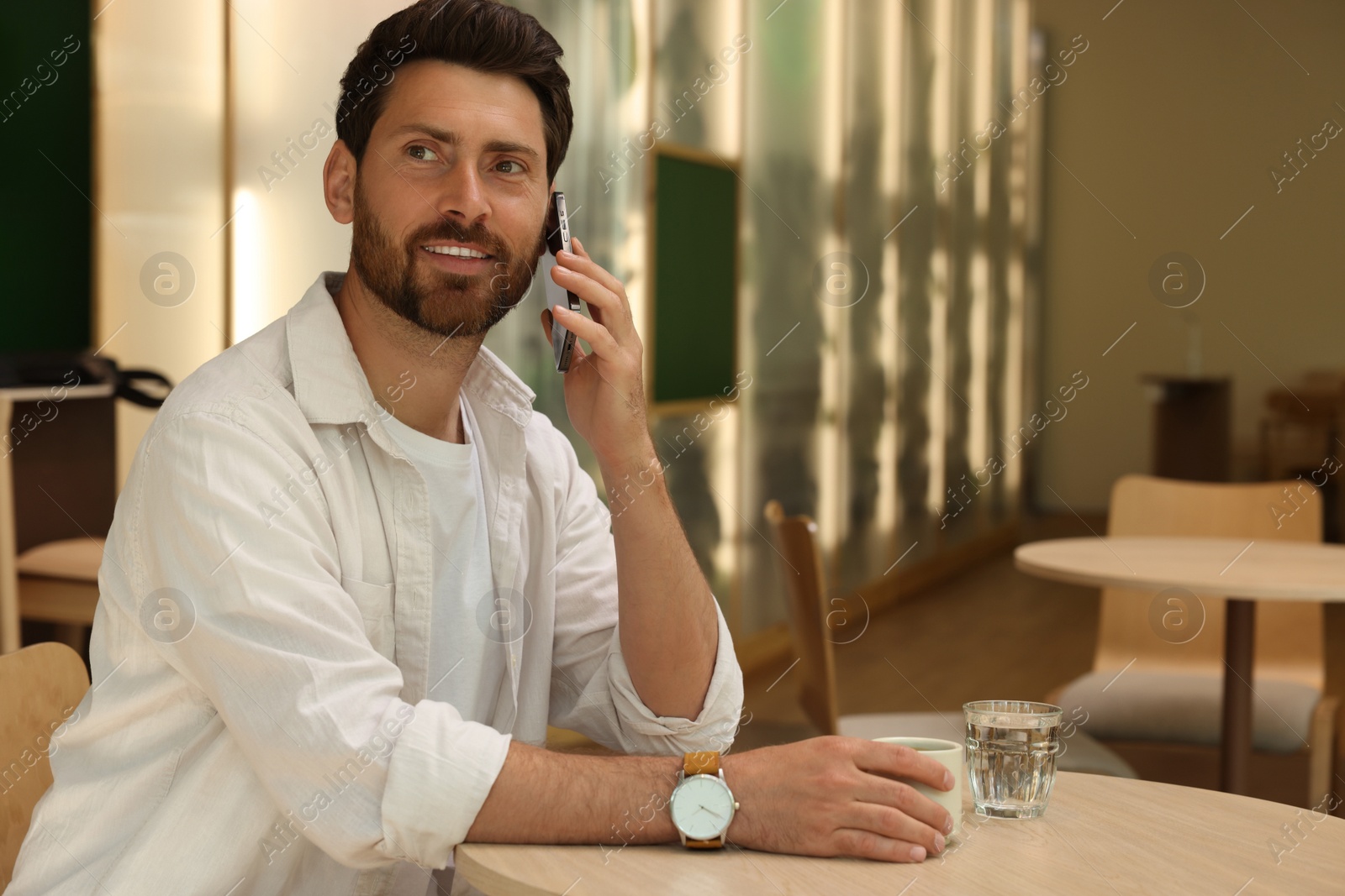 Photo of Handsome man talking on phone at table in cafe