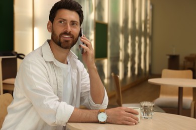 Photo of Handsome man talking on phone at table in cafe