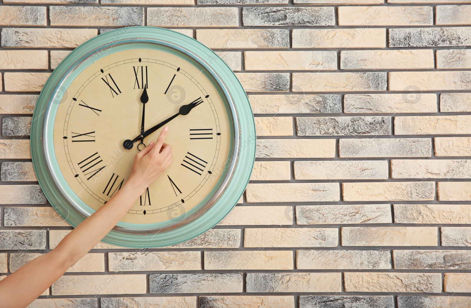 Photo of Woman adjusting time on clock against brick wall background. Time management
