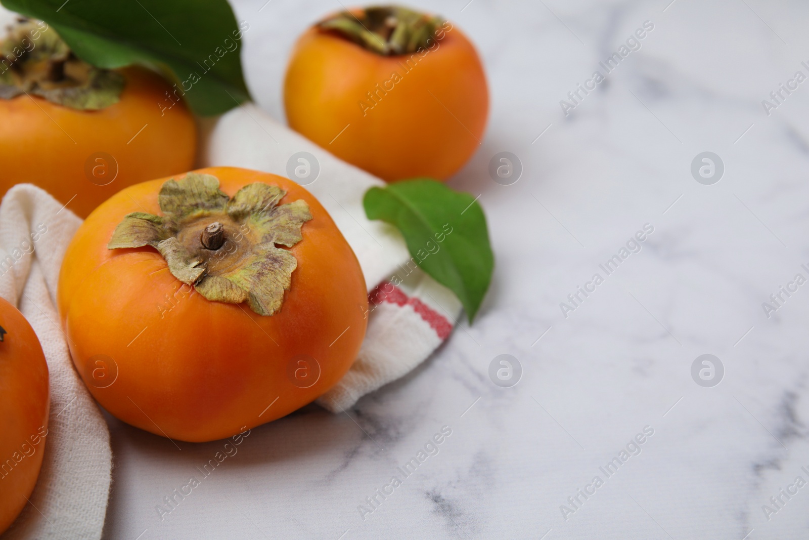 Photo of Delicious ripe juicy persimmons on white marble table. Space for text