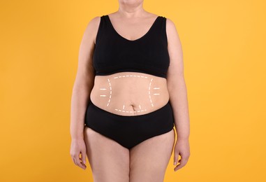 Image of Woman with marks on body before cosmetic surgery operation on orange background, closeup
