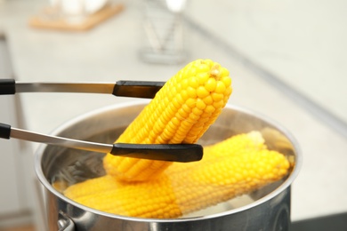 Taking boiled corn from pot with tongs in kitchen, closeup