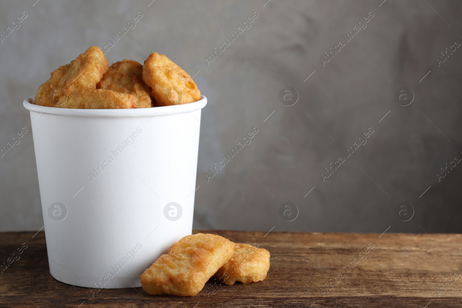 Photo of Bucket with delicious chicken nuggets on wooden table. Space for text