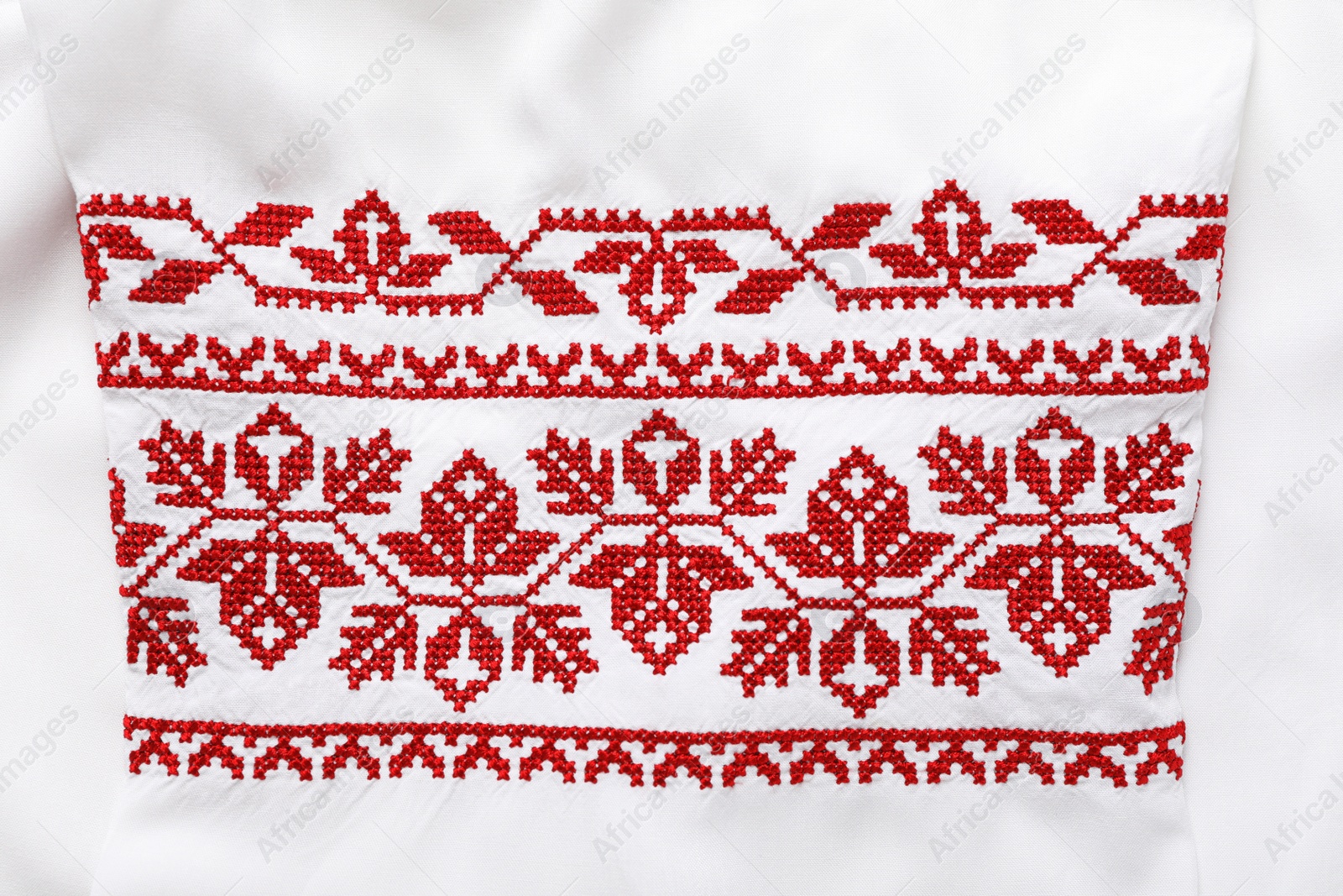 Photo of Beautiful red Ukrainian national embroidery on white fabric, top view