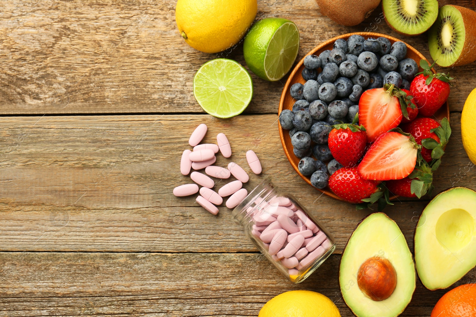 Photo of Vitamin pills in bottle and fresh fruits on wooden table, flat lay. Space for text