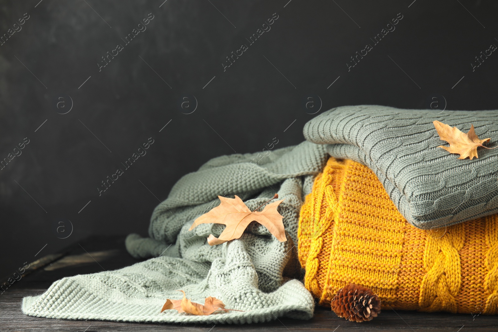 Photo of Different soft plaids, dry leaves and fir cone on black wooden table, closeup