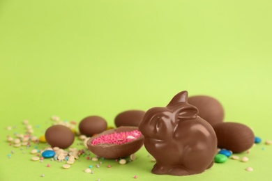 Photo of Chocolate Easter bunny, eggs and candies on green background. Space for text