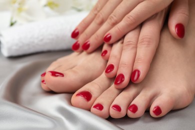 Photo of Woman showing stylish toenails after pedicure procedure and manicured hands with red polish on grey silk fabric, closeup
