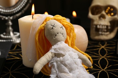 Photo of Voodoo doll pierced with pins and candles on black mat. Curse ceremony