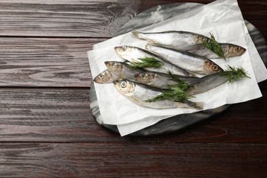 Photo of Fresh raw sprats and dill on wooden table, top view. Space for text