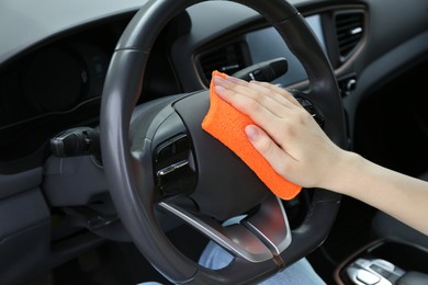 Photo of Woman cleaning steering wheel with rag in car, closeup