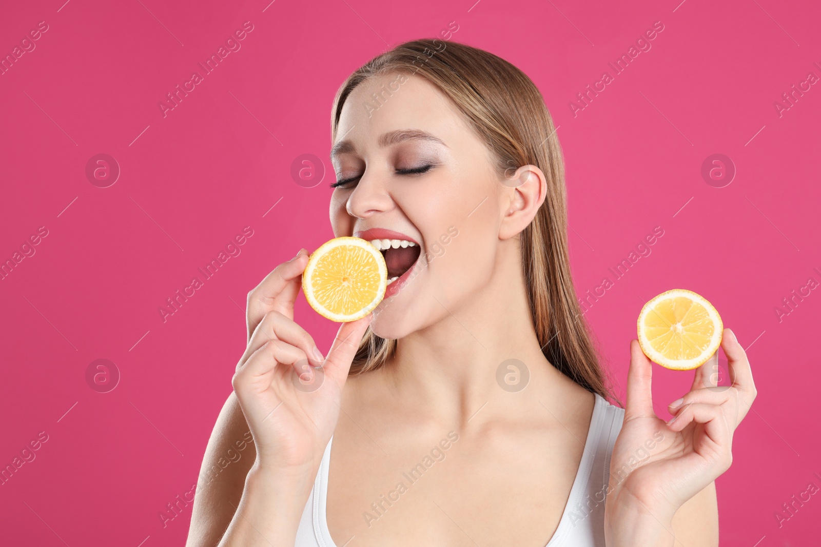 Photo of Young woman with cut lemon on pink background. Vitamin rich food