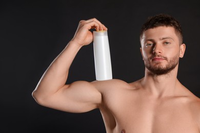 Photo of Shirtless young man holding bottle of shampoo on black background