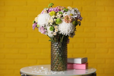 Photo of Bouquet of beautiful chrysanthemum flowers and boxes on white table against yellow brick wall