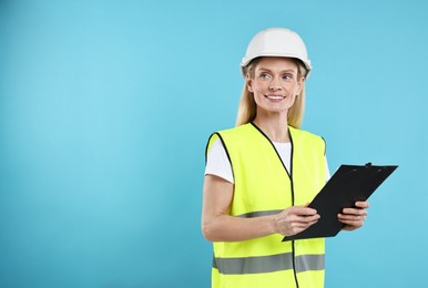 Photo of Engineer in hard hat holding clipboard on light blue background, space for text