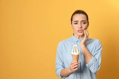 Photo of Emotional young woman with sensitive teeth and ice cream on color background. Space for text