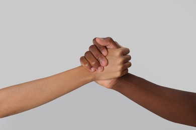 Photo of Woman and African American man clasping hands on light grey background, closeup