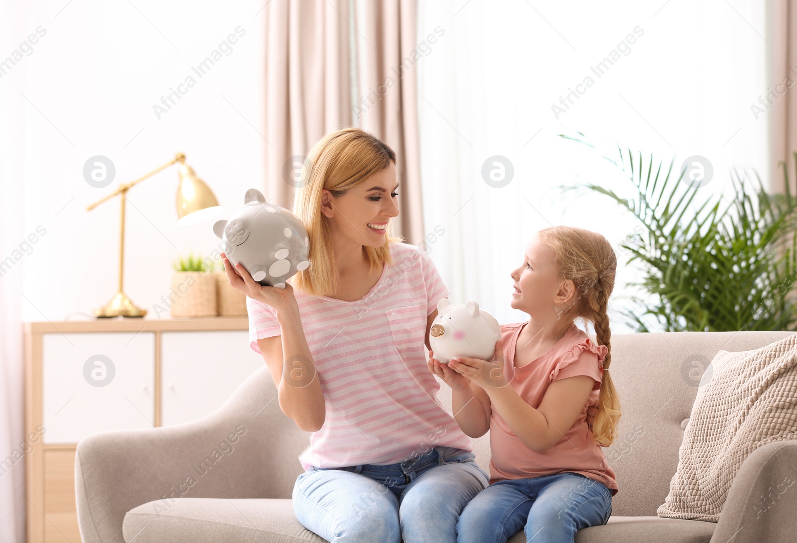 Photo of Mother and daughter with piggy banks at home