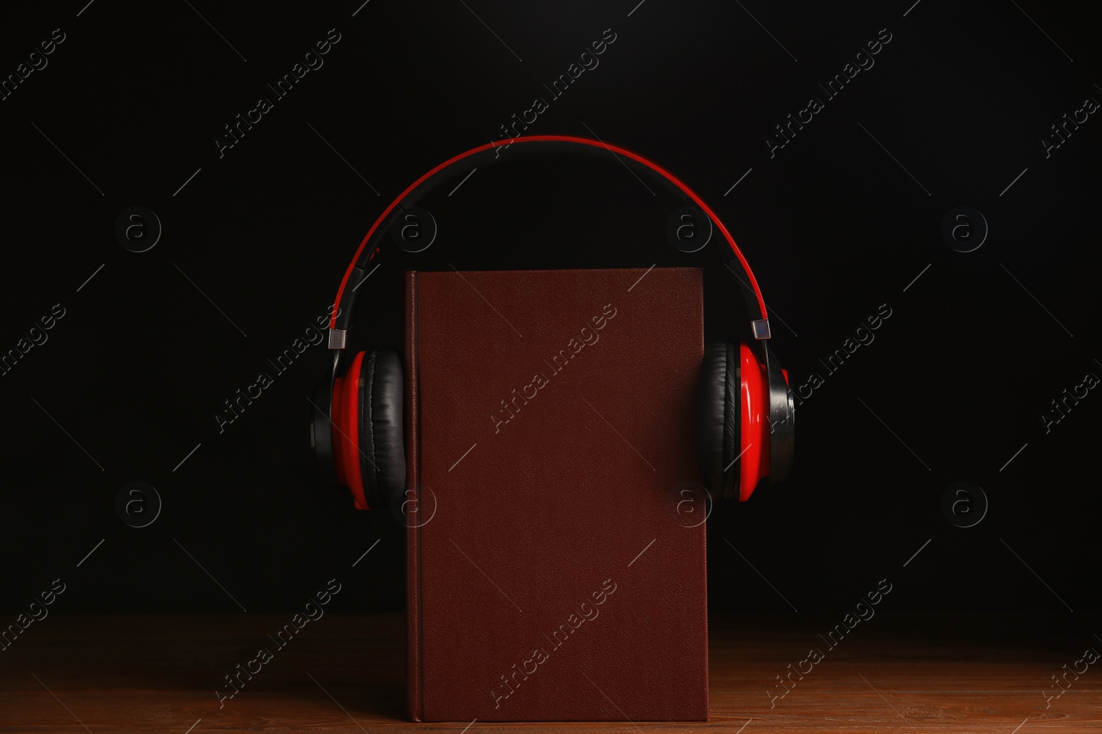 Photo of Headphones and book on wooden table against black background