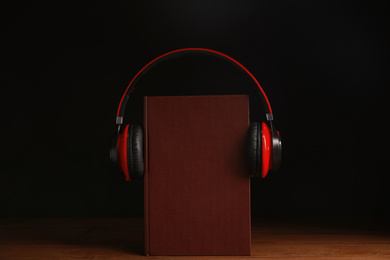 Photo of Headphones and book on wooden table against black background