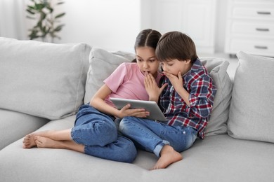 Happy brother and sister with tablet on sofa at home