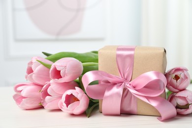 Photo of Beautiful gift box with bow and pink tulips on white table