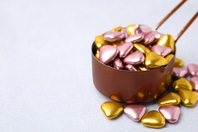 Metal scoop and delicious heart shaped candies on white table. Space for text