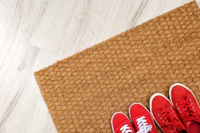 Photo of New clean doormat with shoes on floor, top view. Space for text