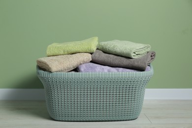 Photo of Plastic laundry basket with clean terry towels on floor near light green wall