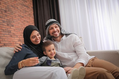 Photo of Happy Muslim family spending time together on sofa at home, space for text