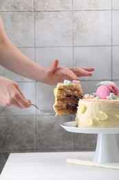 Photo of Woman taking slice of delicious cake at white wooden table, closeup