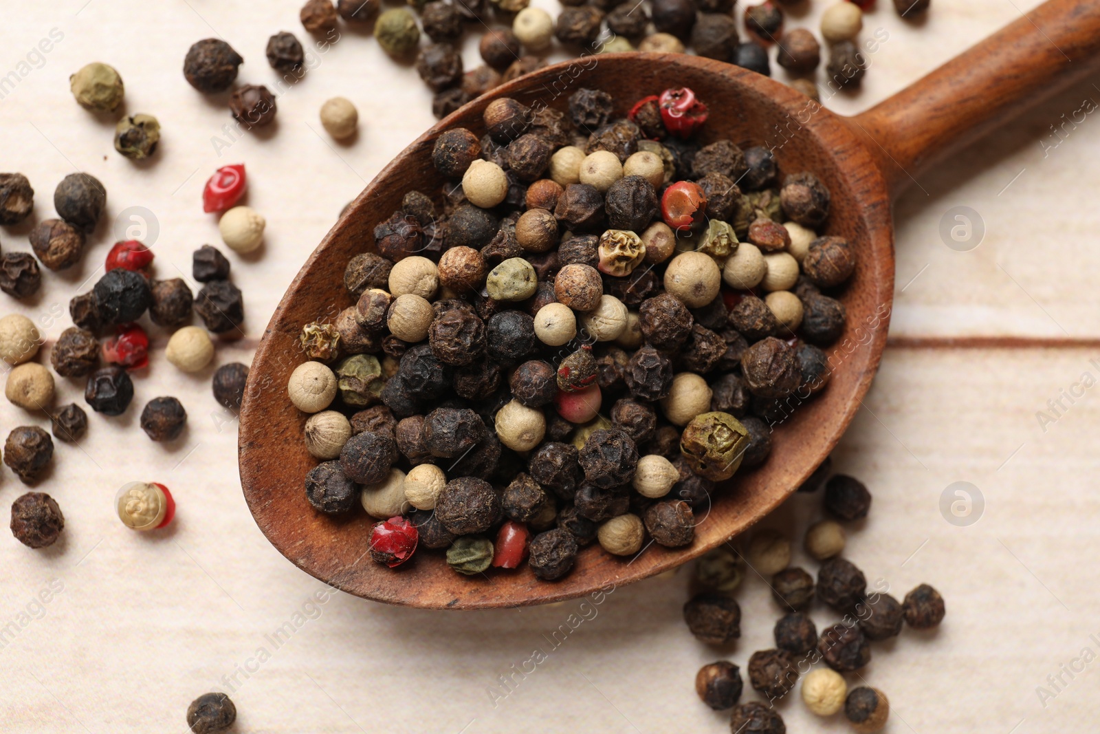 Photo of Aromatic spices. Different peppers in spoon on wooden table, top view