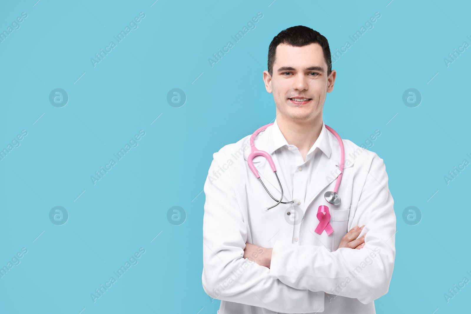 Photo of Portrait of smiling mammologist with pink ribbon and stethoscope on light blue background. Space for text