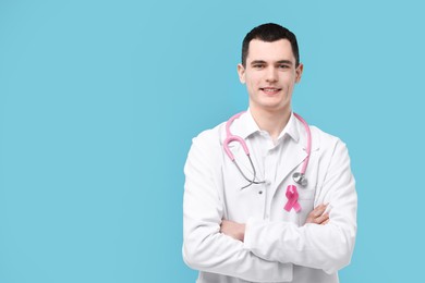 Portrait of smiling mammologist with pink ribbon and stethoscope on light blue background. Space for text