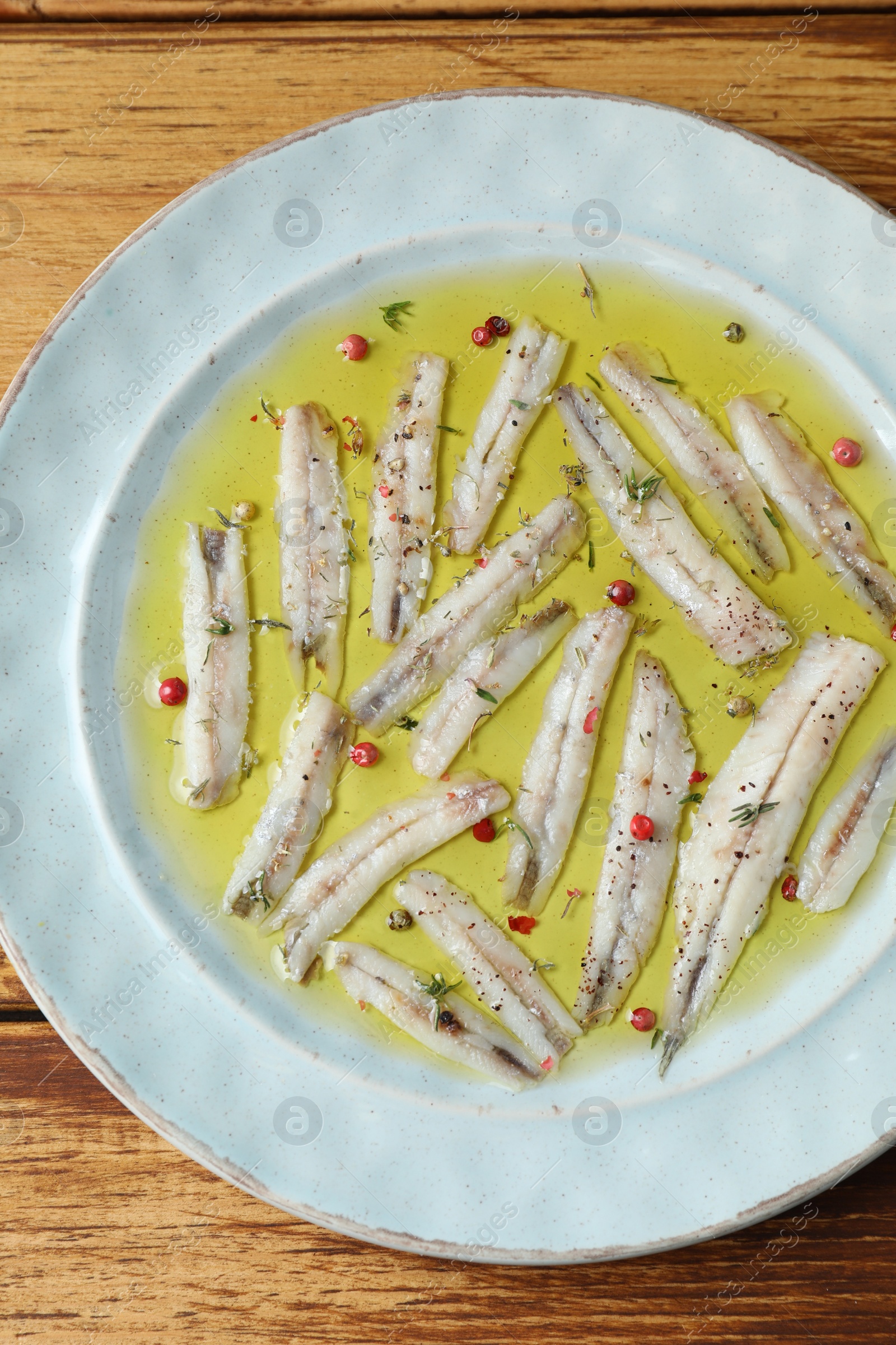 Photo of Tasty pickled anchovies with spices on wooden table, top view