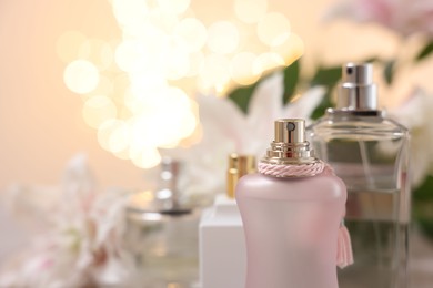 Photo of Bottles of perfume against beautiful lily flowers and blurred lights, closeup. Space for text