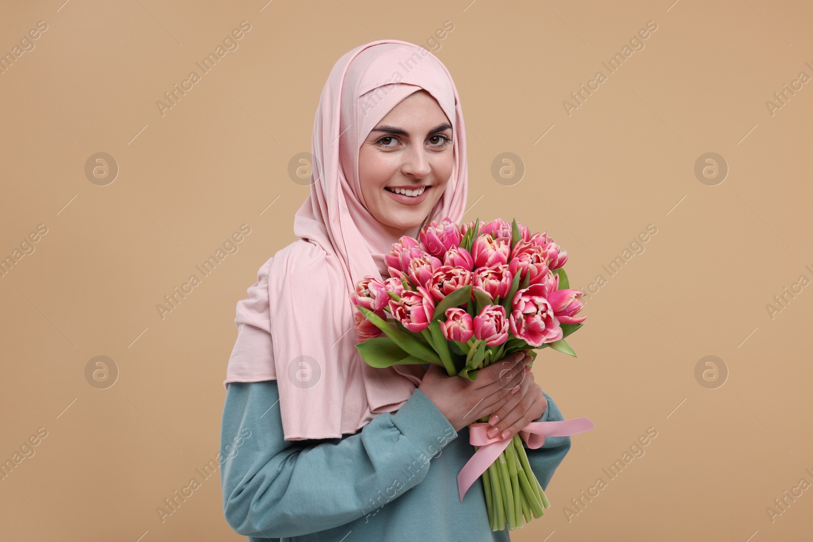 Photo of Happy woman in hijab with beautiful bouquet on beige background