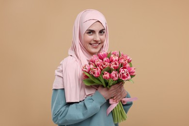 Happy woman in hijab with beautiful bouquet on beige background
