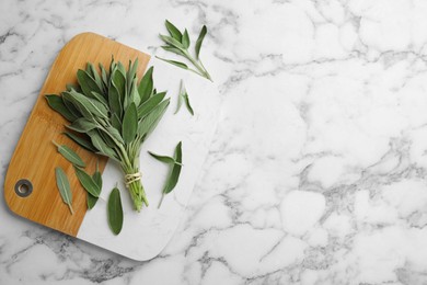 Board with fresh green sage on white marble table, flat lay. Space for text