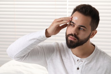 Man with dry skin applying cream onto his forehead indoors