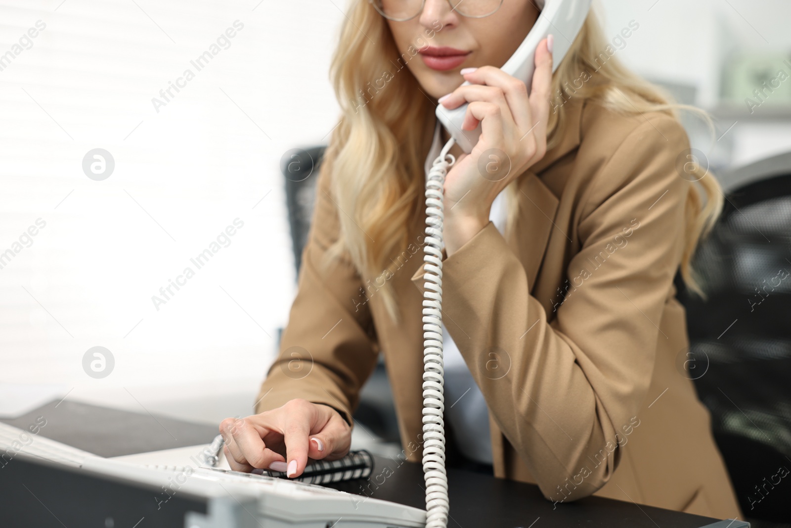 Photo of Secretary talking on phone at table in office, closeup